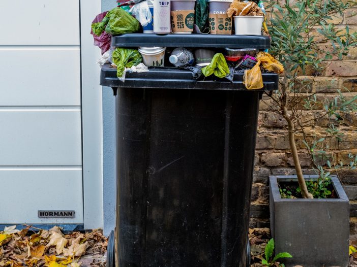 black garbage can overflowing with waste