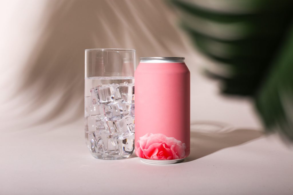 A pink aluminum can next to a refeshing glass of ice