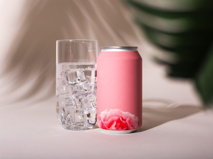 A pink aluminum can next to a refeshing glass of ice