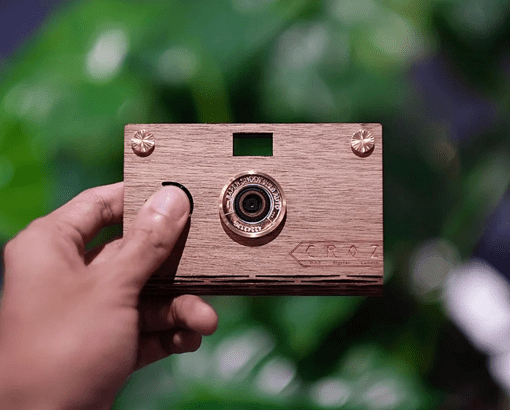 A person holding up a thin, disposal camera that was made from recycled cardboard.