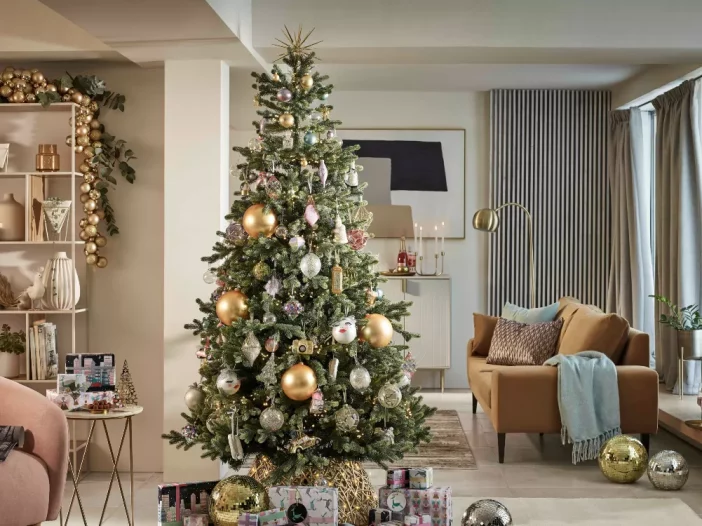 A beautiful Christmas tree inside a cozy home. There are gifts underneath and the decorations are gold and silver.