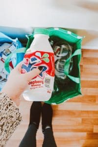 A person is holding an empty milkshake bottle over two recycling bags which are blue and green.